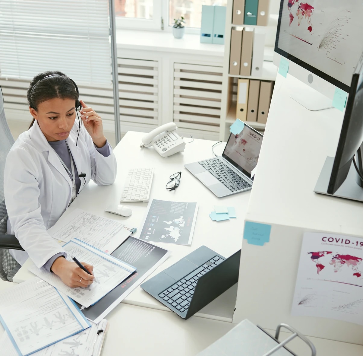 A behavioral health biller working across a laptop and desktop chart review