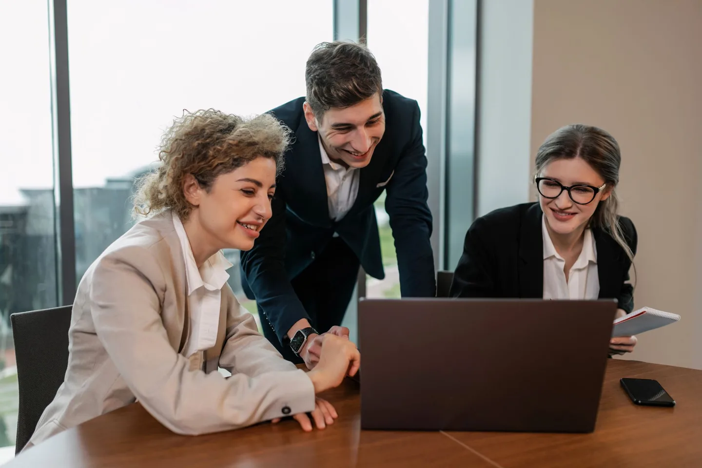 Three professionals collaborating around a laptop in a bright office.